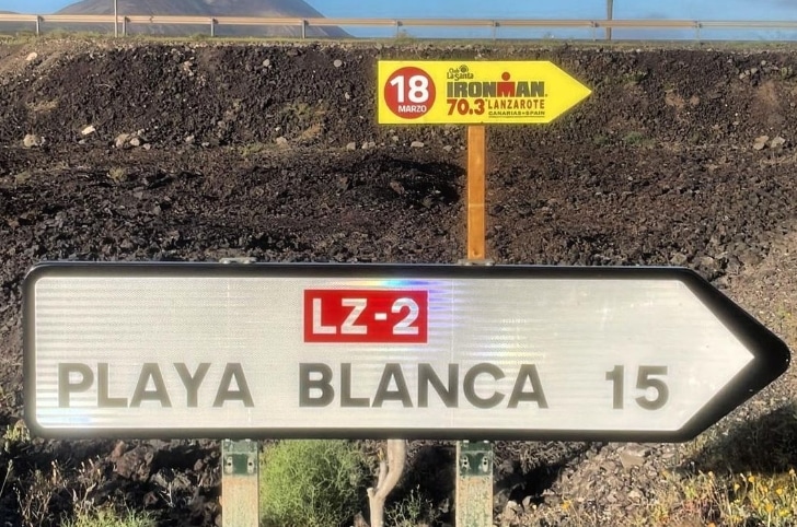 Image of the IRONMAN 70.3 Lanzarote poster and the sign of Playa Blanca