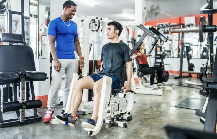 Canva: A personal trainer and his student on the adductor and adductor machine