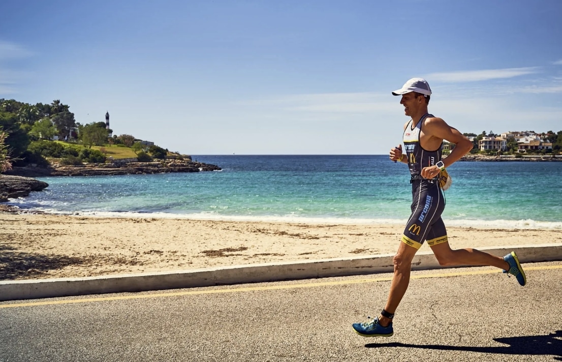 Un triatleta corriendo en Portocolom con el faro de fondo