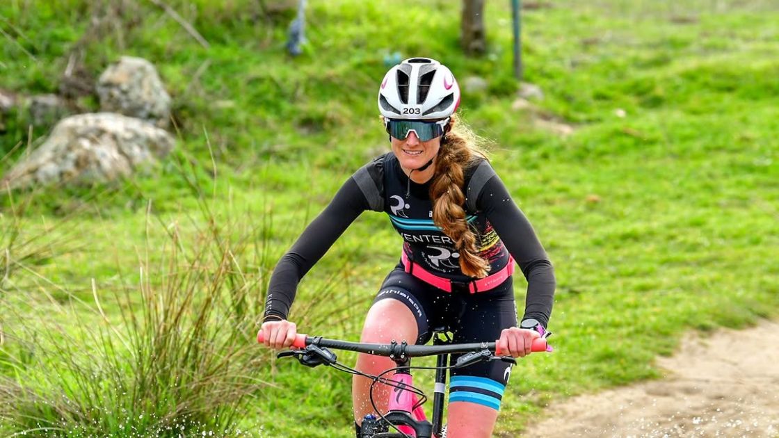 Triatleta compitiendo en el segmento de bicicleta durante una prueba de duatlón cross sobre terreno natural.
