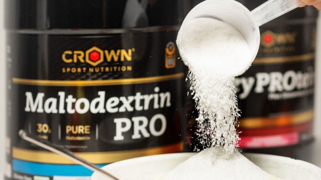 Maltodextrin PRO de Crown Sport Nutrition con dosificador vertiendo polvo