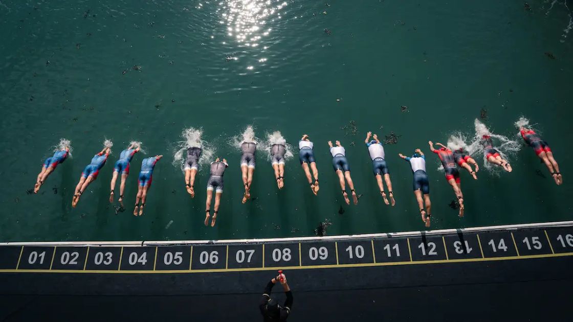 Salida de natación con triatletas profesionales lanzándose al agua en una prueba Supertri Título de la imagen Inicio del segmento de natación en una carrera Supertri