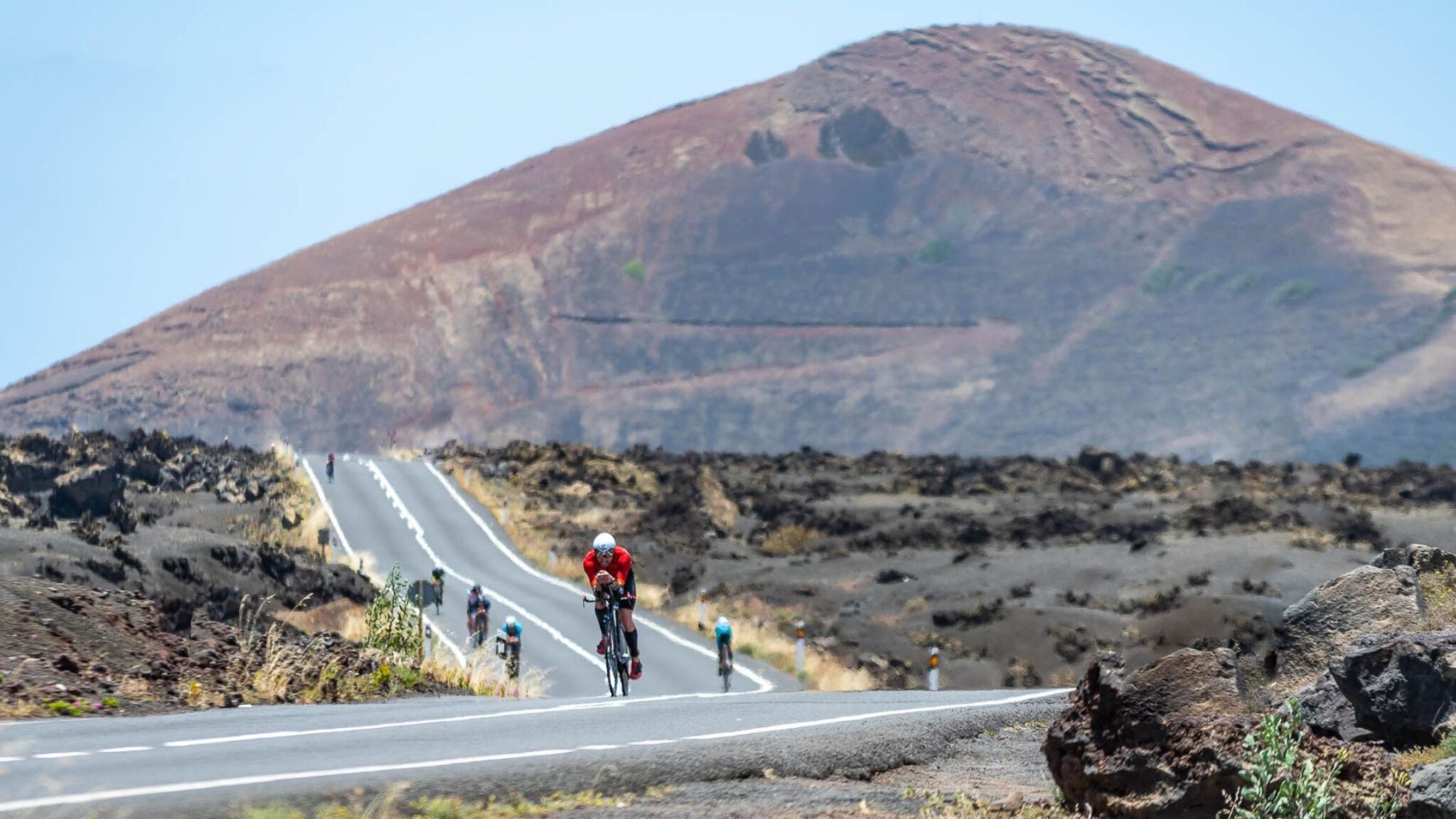 Triatletas compitiendo en bicicleta en el paisaje volcánico de Lanzarote durante la Copa del Mundo de Triatlón