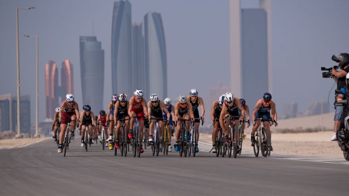 Pelotón de triatletas en el segmento ciclista de la WTCS Abu Dhabi con el skyline de la ciudad al fondo