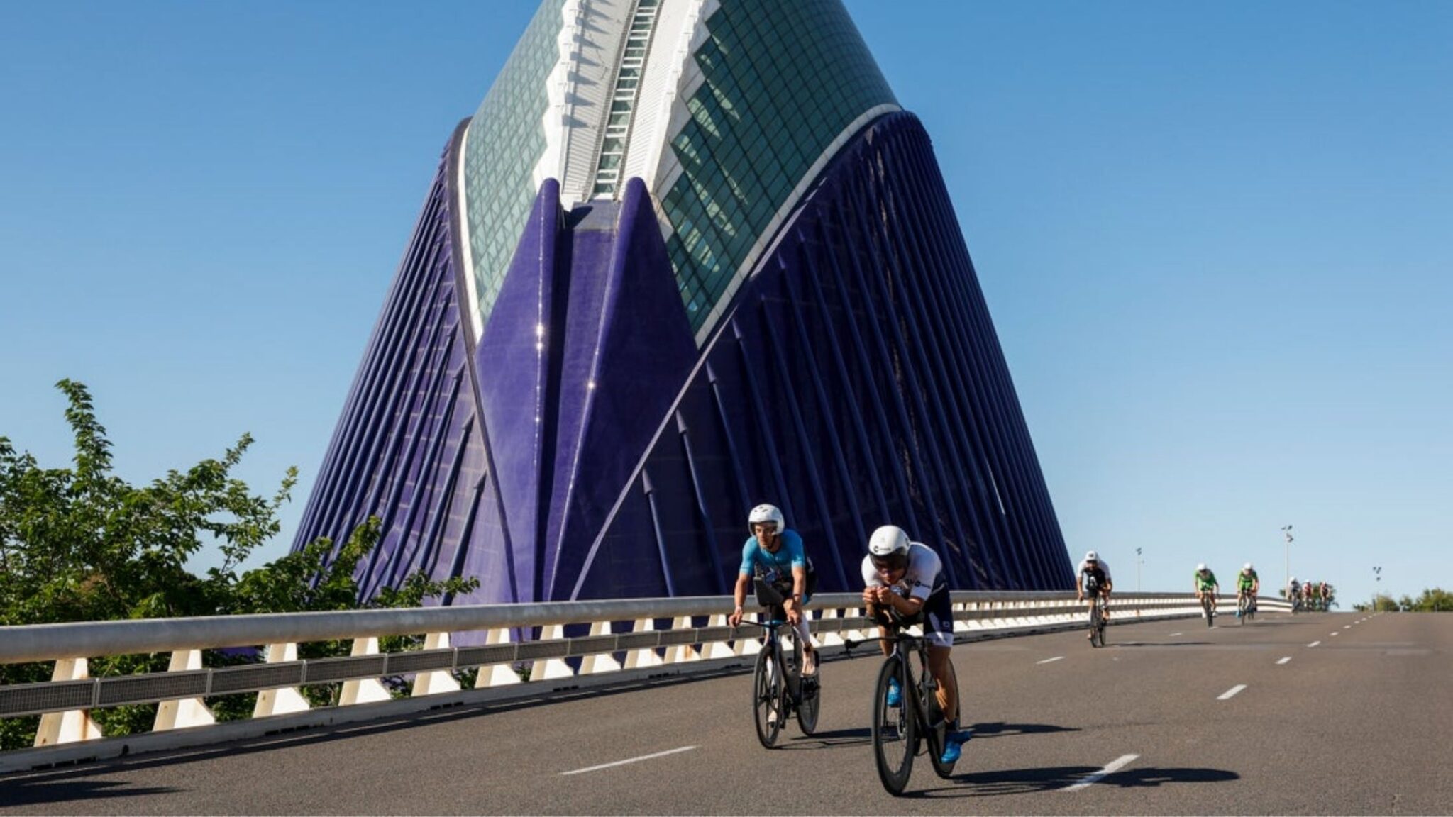 Ciclistas compitiendo en el segmento de bici del IRONMAN 70.3 Valencia junto al edificio Veles e Vents
