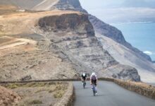 Two triathletes cycle up a road next to the cliffs of Lanzarote