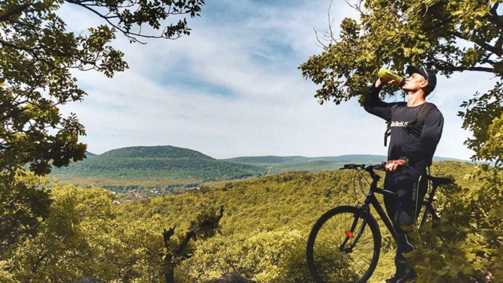 Triatleta bebiendo una bebida isotónica junto a su bicicleta en una ruta de montaña