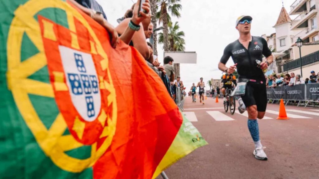 Triatleta corriendo junto a una bandera de Portugal en el IRONMAN Portugal-Cascais