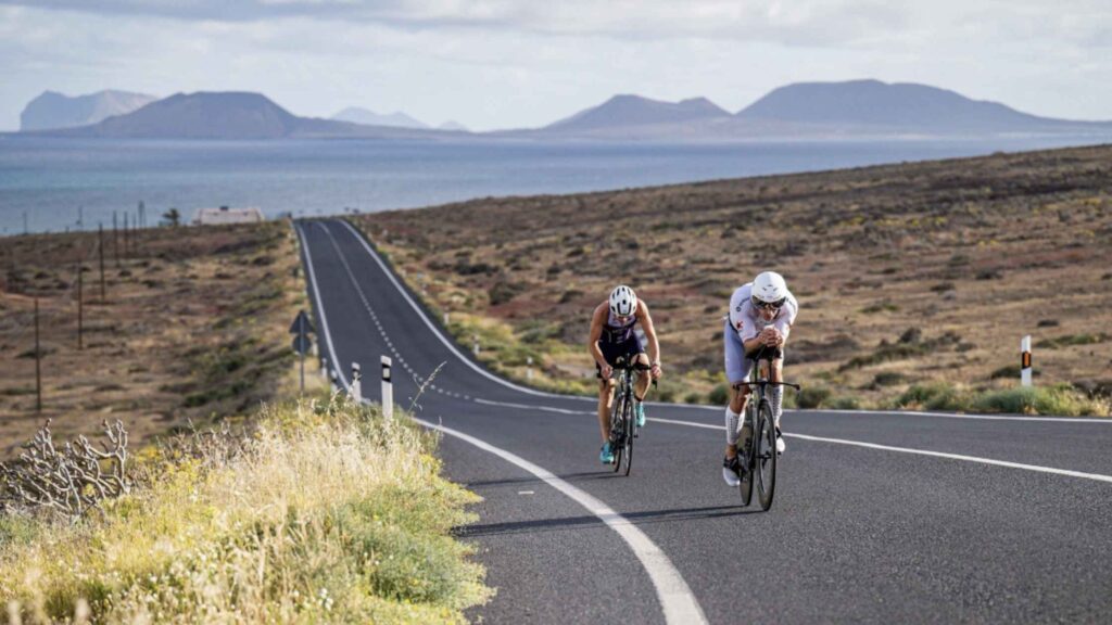 Dos triatletas pedalean por una carretera volcánica de Lanzarote durante el Volcano Triathlon