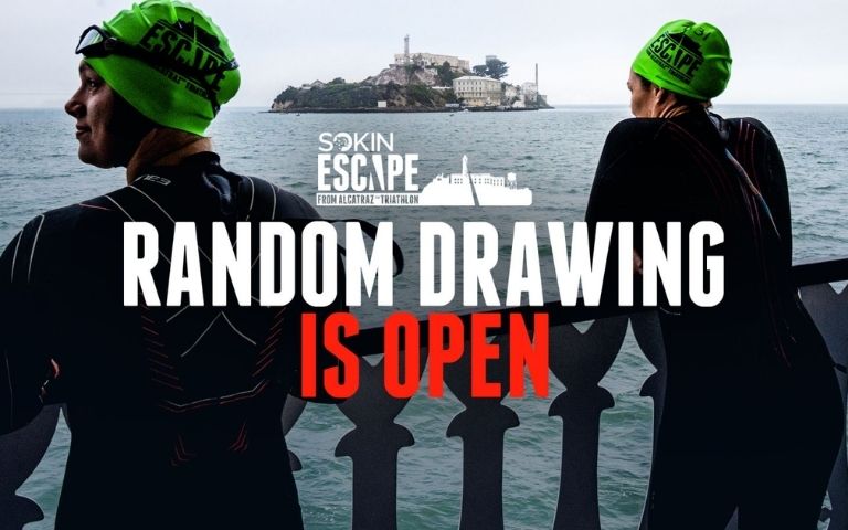 Dos participantes del Escape From Alcatraz junto a la bahía de San Francisco con la isla de Alcatraz al fondo y el anuncio del sorteo de dorsales 2027