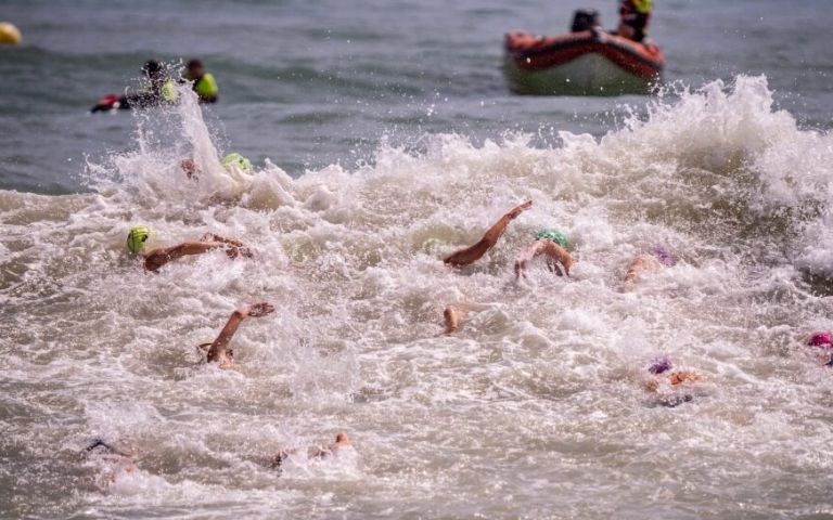 Triatletas nadando entre el oleaje en una prueba de triatlón en mar abierto