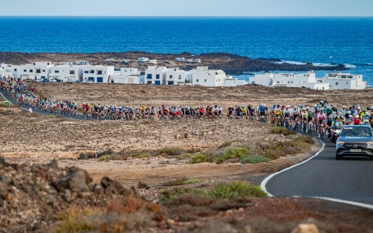 Pelotón de la Vuelta Ciclista a Lanzarote recorriendo una carretera junto a la costa