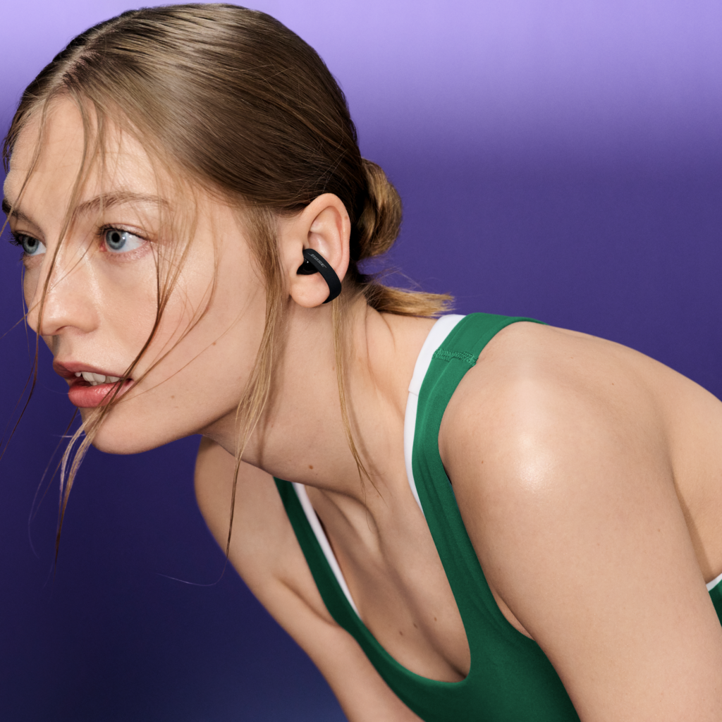 Mujer con ropa deportiva verde que lleva un auricular Bose Sport Open negro de diseño abierto.