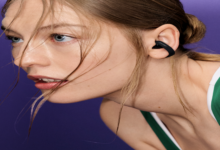 Mujer con ropa deportiva verde que lleva un auricular Bose Sport Open negro de diseño abierto.