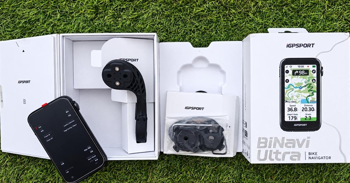 Unboxing del iGPSPORT BiNavi Ultra con ciclocomputador, soporte, accesorios y caja sobre césped