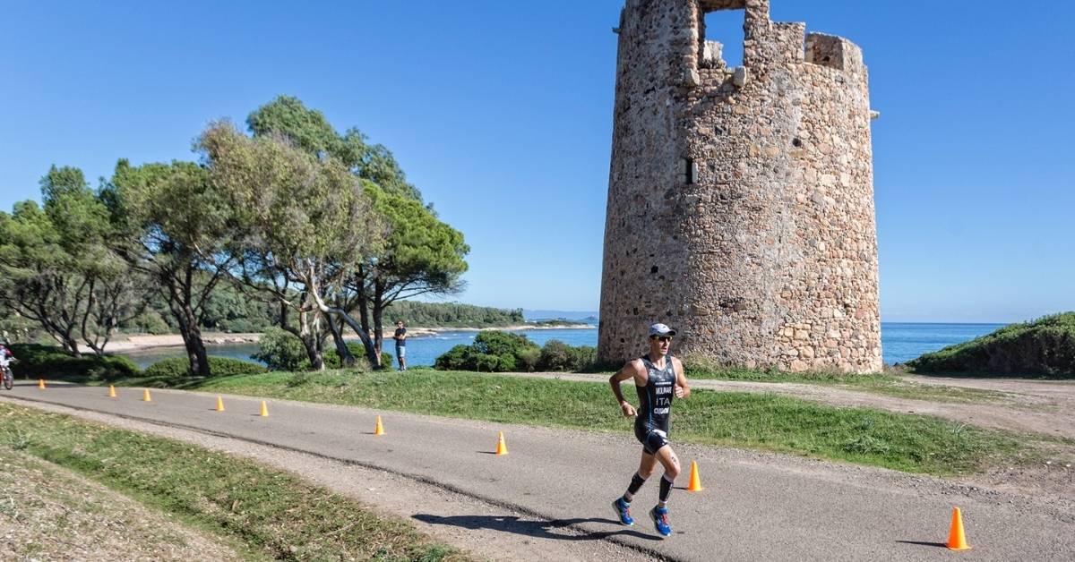 Triatleta corriendo junto a una torre de piedra en la costa de Cerdeña, escenario del Challenge Forte Village Sardinia