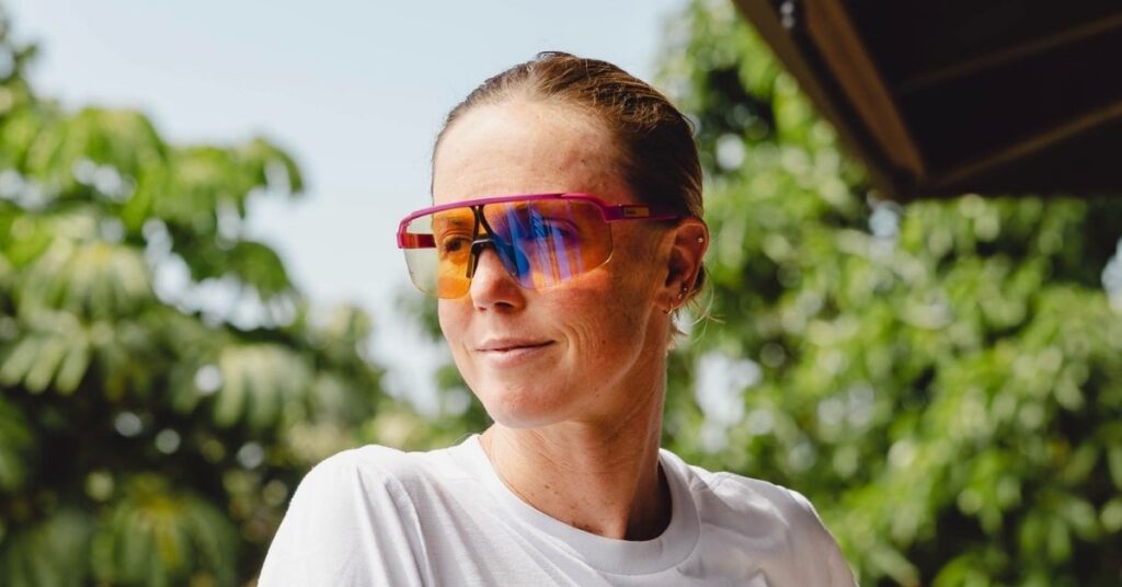 Chelsea Sodaro con gafas deportivas de lentes multicolor y camiseta blanca, en un retrato al aire libre