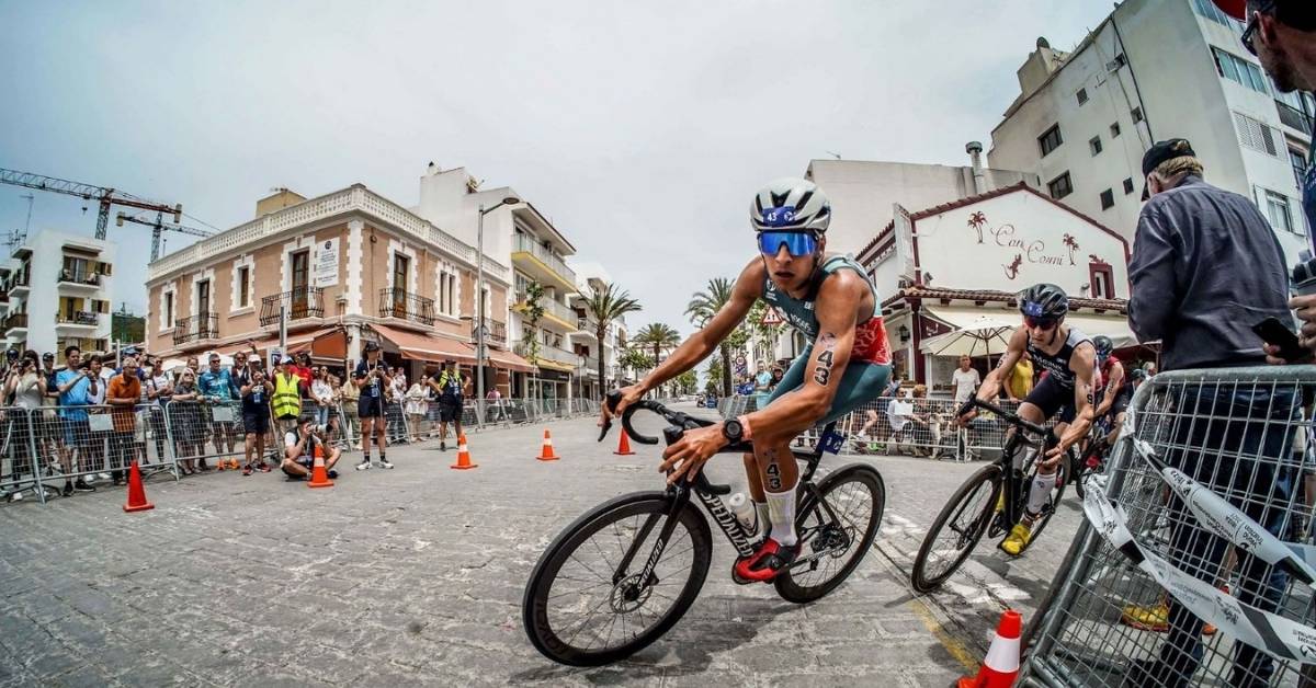 Triatletas toman una curva en bicicleta durante una competición de triatlón, con público junto al circuito