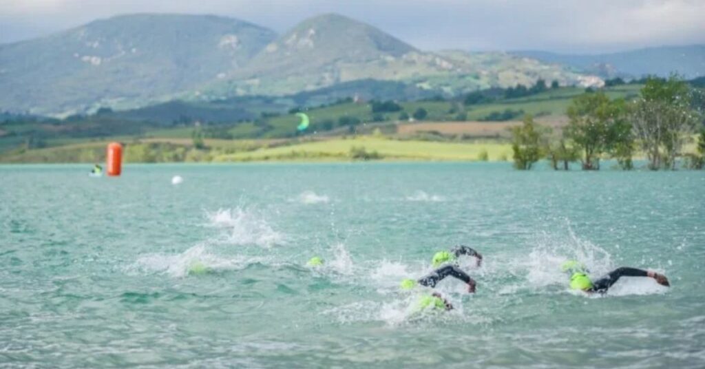 Triatletas nadando en aguas abiertas durante una competición en Pamplona, con montañas al fondo
