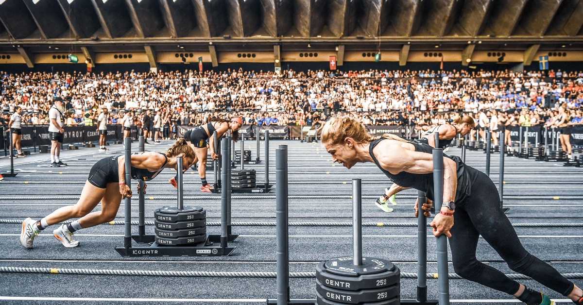 Participantes de HYROX empujan trineos con peso durante una competición de fitness híbrido en un pabellón lleno de público