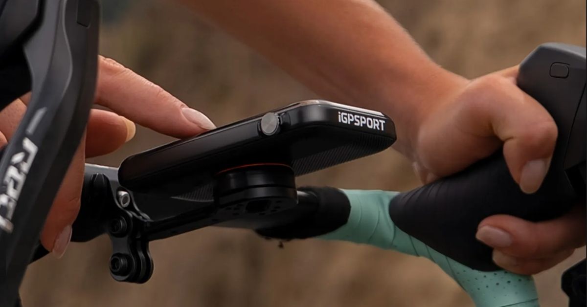 Detalle lateral del iGPSPORT BiNavi Ultra instalado en el manillar de una bicicleta, con su mando giratorio y un dedo junto al control