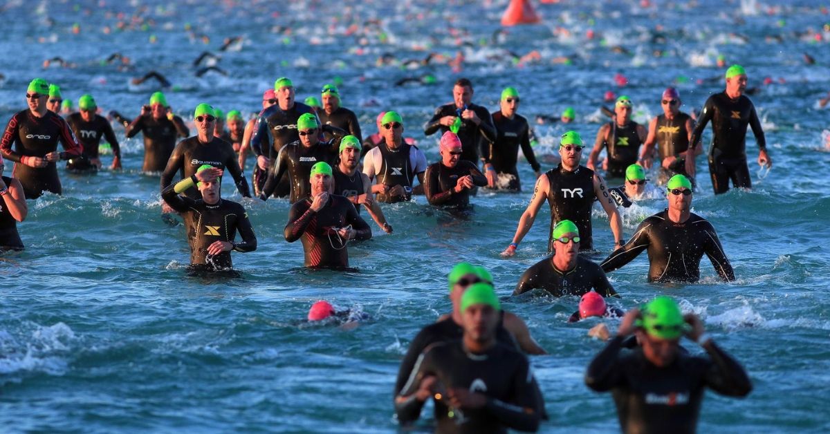 Grupo de triatletas con neopreno y gorros de colores entrando al agua durante una prueba de natación