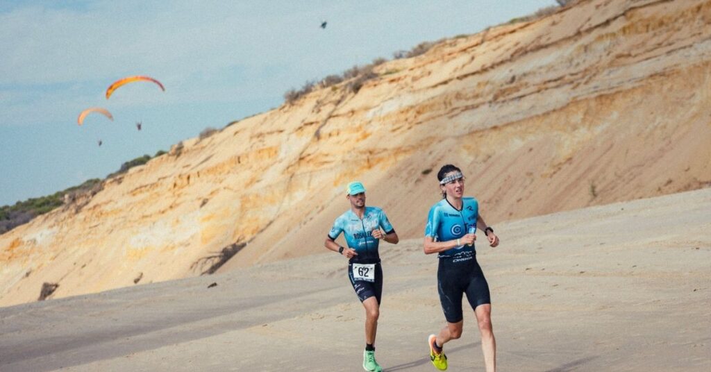 Dos triatletas corren por la playa junto a los acantilados de Matalascañas durante el Desafío Doñana