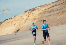 Dos triatletas corren por la playa junto a los acantilados de Matalascañas durante el Desafío Doñana