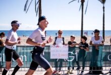 Dos triatletas corren junto a la playa durante un IRONMAN 70.3, animados por espectadores tras las vallas